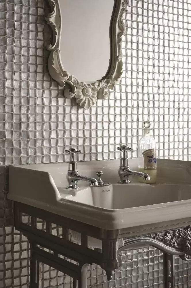 A mirror placed on a wall of textured tiles. Below it is a sink.